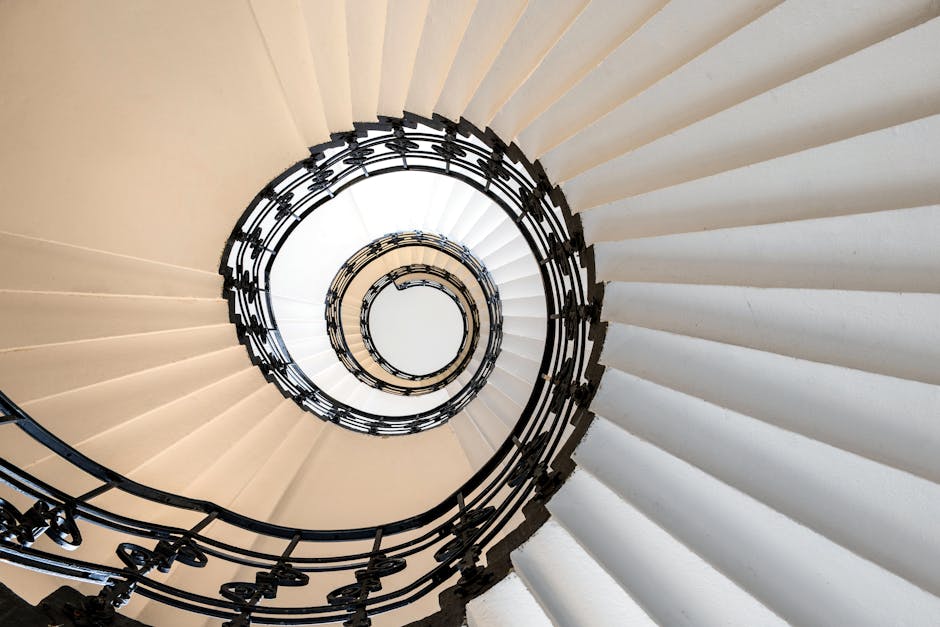 A narrow outdoor staircase with stone steps leading upward between two tall, enclosed walls—one on the left with a black metal railing and a temporary construction barrier, and one on the right with